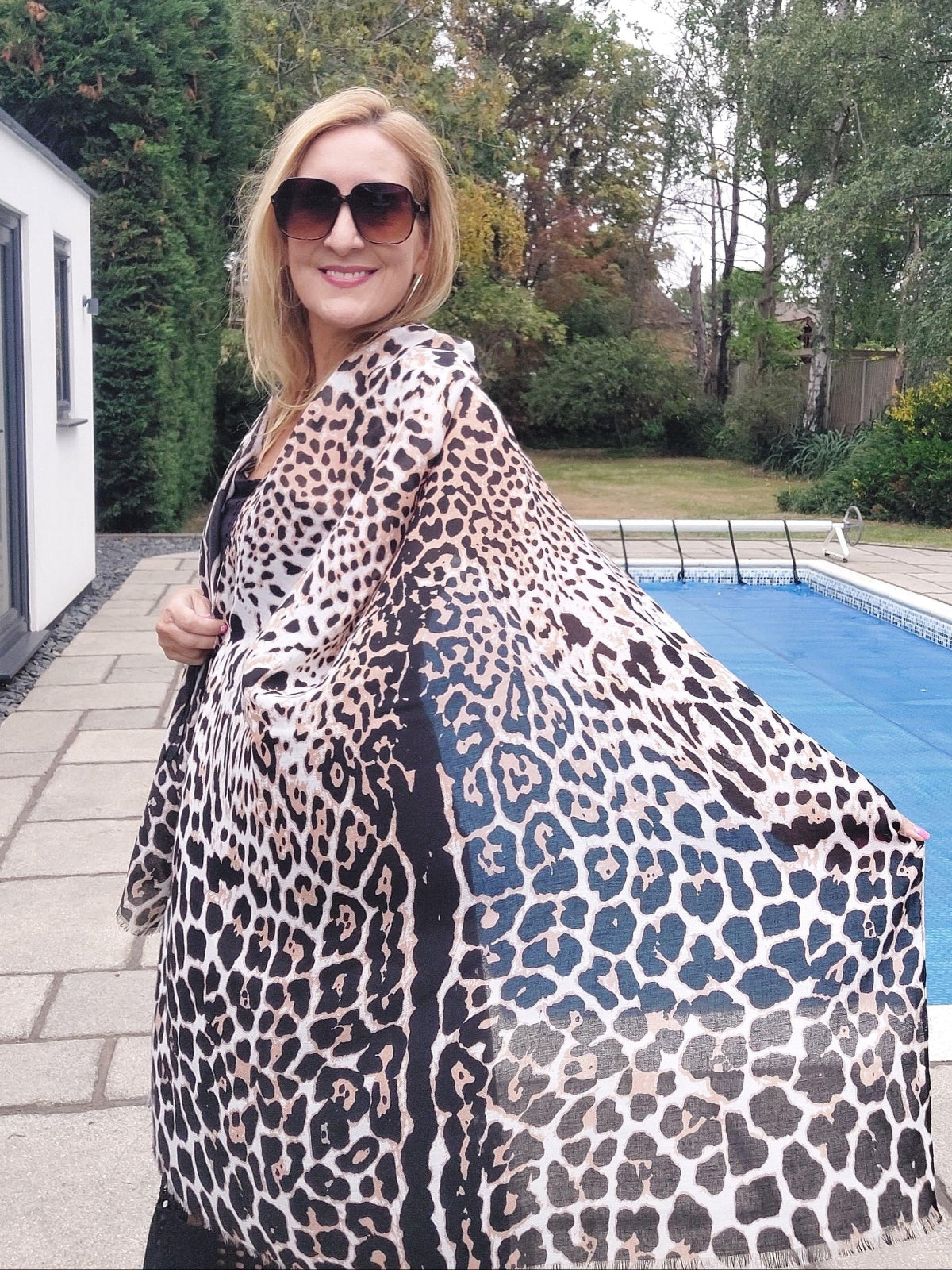 Woman wearing a leopard print scarf outdoors with trees and a building in the background