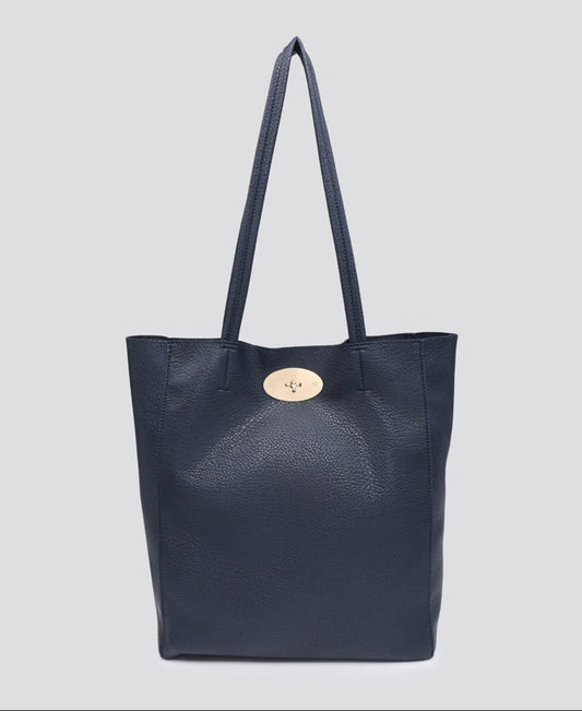 A navy blue pebbled leather tote bag with dual shoulder straps and a signature oval gold-tone button closure, shown against a solid light gray background.