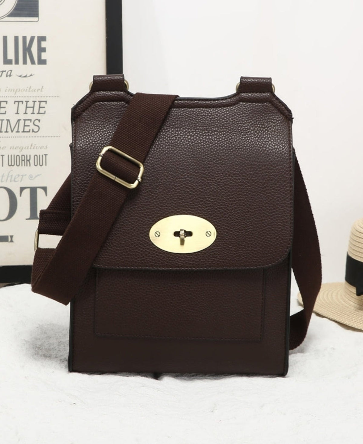Brown leather bag with gold buckle on a white background with a hat and camera poster.