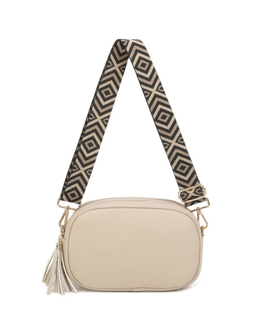 A small oval shoulder bag in light beige with a wide, patterned strap featuring black and beige geometric designs, finished with gold-tone hardware and a matching tassel.