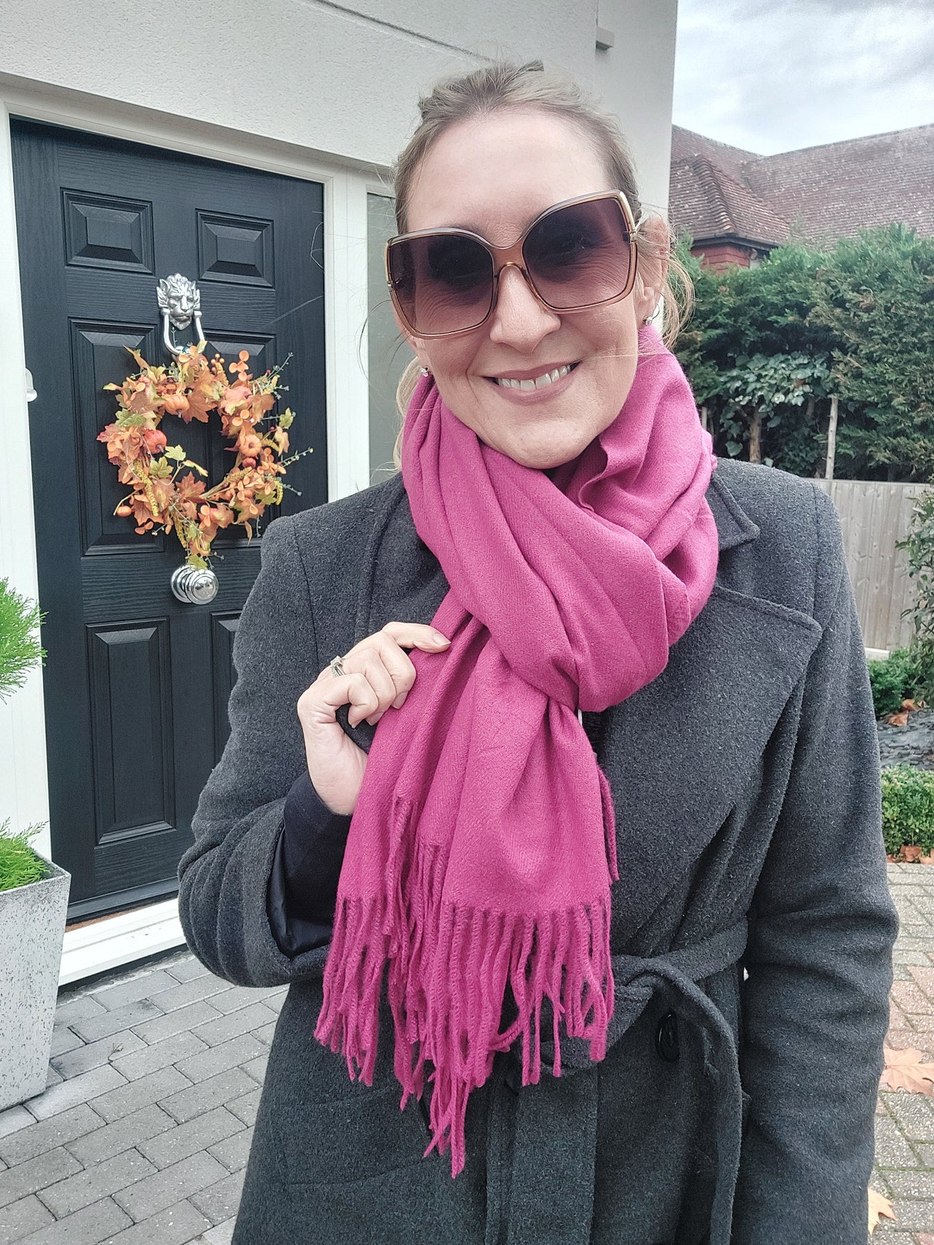 Person wearing a pink scarf and sunglasses, standing in front of a door with a wreath.
