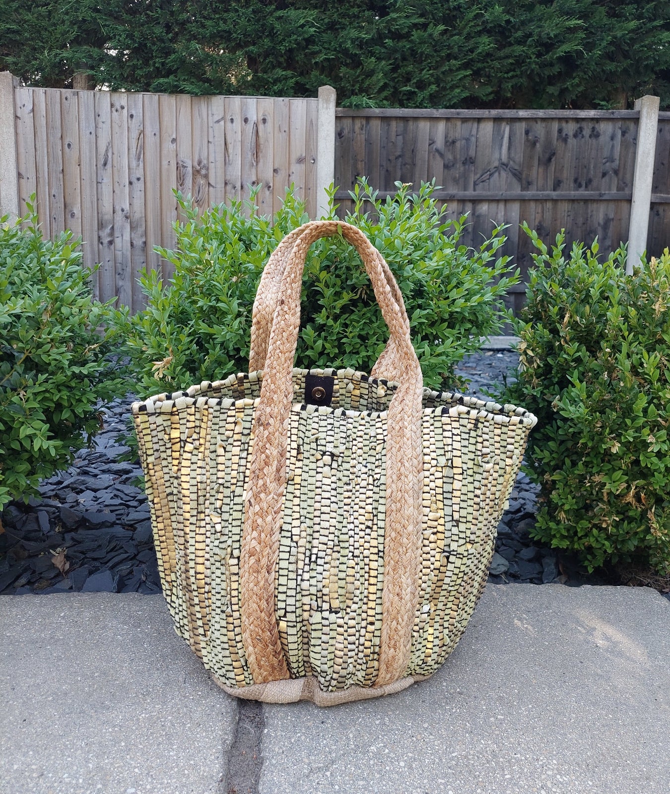 Woven handbag on a stone surface with greenery in the background